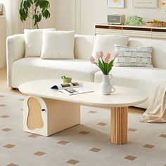 a living room with white couches and a coffee table in the middle, surrounded by potted plants