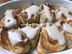 a white bowl filled with cinnamon rolls covered in icing