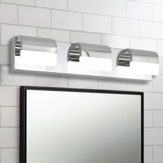 a bathroom mirror with three lights on it and a white tiled wall in the background