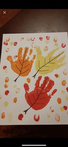 an art project with hand prints and leaves painted on white paper, sitting on top of a wooden table