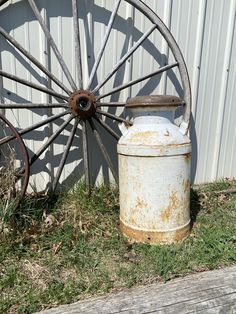 an old rusted water can sitting next to a wagon wheel