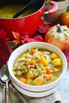 a white bowl filled with soup next to some silver spoons and an orange pumpkin