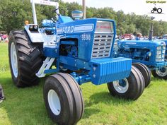 an old blue tractor is parked on the grass in front of other antique tractors and people