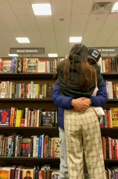 two people hugging each other in front of a bookshelf filled with lots of books