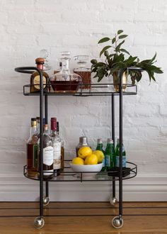 a bar cart with drinks and liquor bottles on it in front of a white brick wall