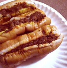 two hotdogs on a paper plate with mustard and ketchup in the middle