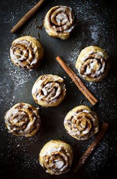 cinnamon rolls with icing and cinnamon sticks on a black surface next to cinnamon sticks