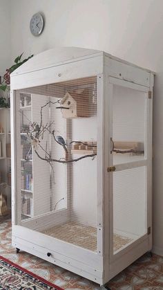 a white bird cage sitting on top of a rug next to a clock and bookshelf