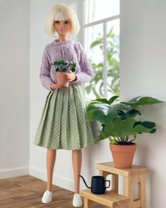 a doll is standing next to a potted plant and holding a flower in her hands