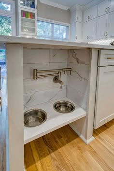 an open cabinet in the middle of a kitchen with stainless steel sinks and faucets