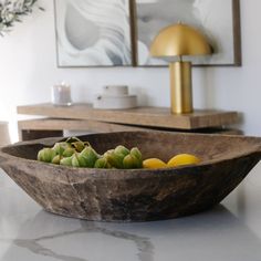 a wooden bowl filled with fruit sitting on top of a counter next to a lamp