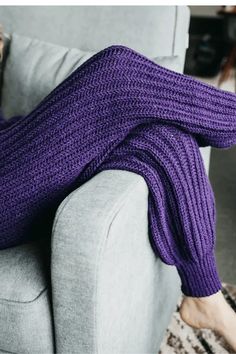 a woman laying on top of a couch covered in a purple blanket