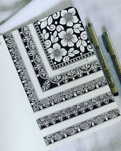 an open notebook with black and white designs on it next to two markers, pencils and a pen