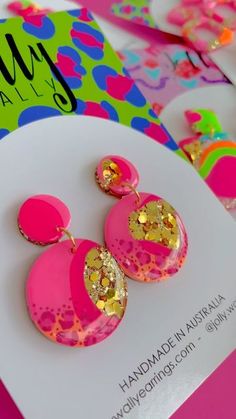 the pink and gold earrings are sitting on top of a white card next to other items