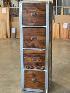 a metal and wood filing cabinet with three drawers in a warehouse or storage area on concrete flooring