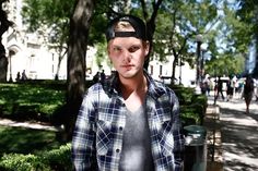 a man standing in the middle of a park wearing a hat and looking at the camera