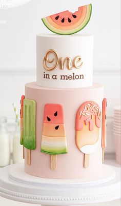 a pink cake with popsicles and watermelon slices on the top that says one in a melon