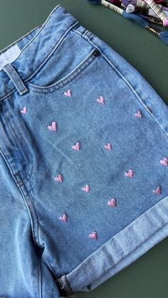 a pair of blue jean shorts with pink hearts on them next to crayons