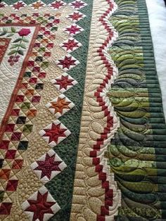 a quilted table runner with green, red and white designs on the edge is laying on a bed