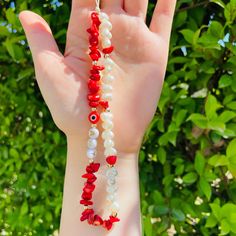 a hand is holding some red and white beads on it's palm, with green leaves in the background