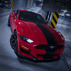 a red sports car with black stripes parked in a parking garage next to yellow and white striped barriers