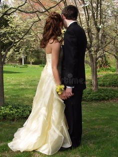 a bride and groom kissing in front of trees with flowers on their wedding day at the park