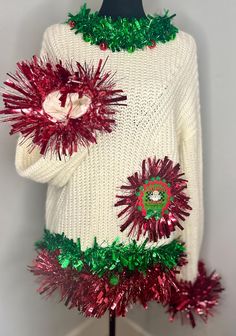 a white sweater with red and green tinsels on the bottom, attached to a mannequin head