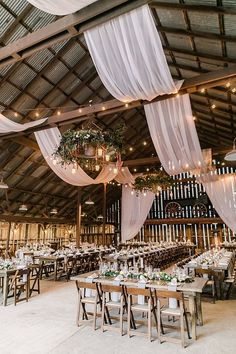 the inside of a barn with tables and chairs set up for a wedding reception, decorated with white draping