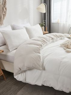 an unmade bed with white linens and pillows in a bright room next to a window