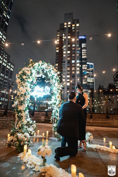 a man and woman sitting next to each other in front of some tall buildings at night