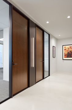 an empty room with two wooden doors and pictures on the wall behind them in front of glass windows