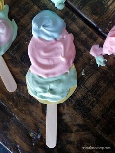 three popsicles with different colored frosting on top of each other, sitting on a wooden table