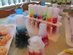 there are many different colored liquids in test tubes on the table next to cookies and cupcakes