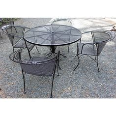 an outdoor table and chairs are set up on the gravel ground with trees in the background