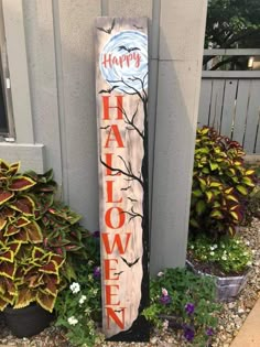 a wooden sign that says happy halloween in front of some flowers and plants on the side of a house