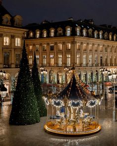 a merry go round in front of a large building with christmas lights on the trees