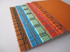 four different colored notebooks sitting on top of each other, one is orange and the other is blue