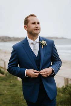 a man in a blue suit is standing by the beach