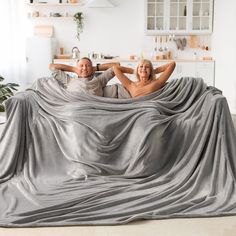 a man and woman laying on top of a couch covered in a blanket