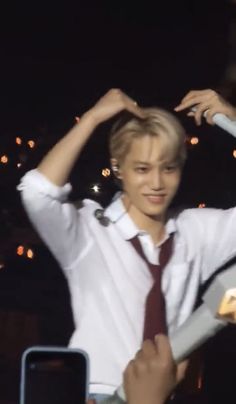 a young man wearing a white shirt and tie holding his hands up to his head