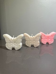 three candles are sitting on a table with one candle in the shape of a butterfly