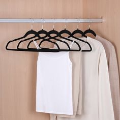 three white shirts hanging on a clothes rack with black hangers and two beige ones