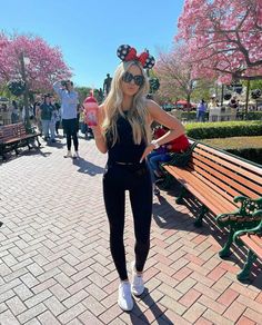 a woman wearing minnie mouse ears standing in front of a park bench