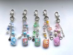 several key chains with different designs and colors are on a white surface, one has a phone charm hanging from it's side