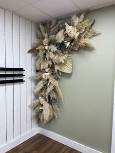 an arrangement of dried flowers on the wall in a room with white walls and wood flooring