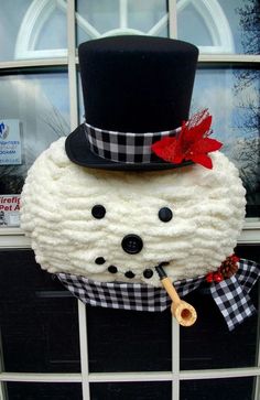 a snowman made out of yarn with a top hat and cane in front of a window