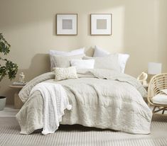 a bed with white linens and pillows in a neutral colored room next to a wicker chair