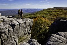 two people standing on the edge of a cliff with their backs to each other, overlooking mountains