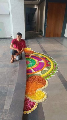 a man sitting on the ground next to a large flower arrangement in front of a building