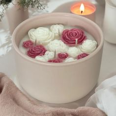 a white bowl filled with pink and white flowers next to a candle on a table